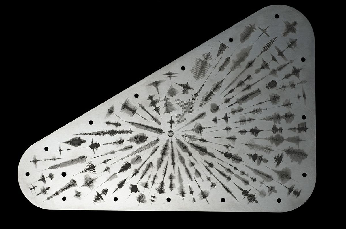 a triangular silver object etched with a variety of symbols is shown against a black background